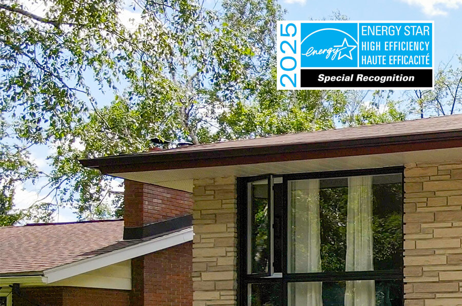 Part of a house roof with brick and stone exterior and large windows. In the sky, theres a 2025 ENERGY STAR High Efficiency Special Recognition badge. Green trees are visible in the background.